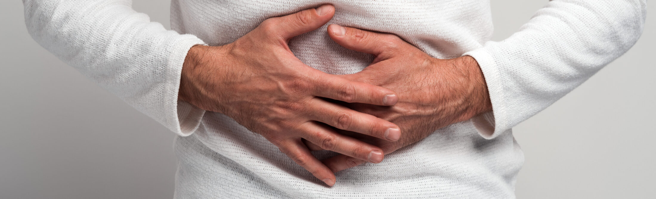 Close up view of the man holding hands on stomach feeling acute pain, suffering indigestion and nausea, duodenal ulcer. Indoor studio shot isolated on white background Close up view of the man holding hands on stomach feeling acute pain, suffering indigestion and nausea, duodenal ulcer. Indoor studio shot isolated on white background