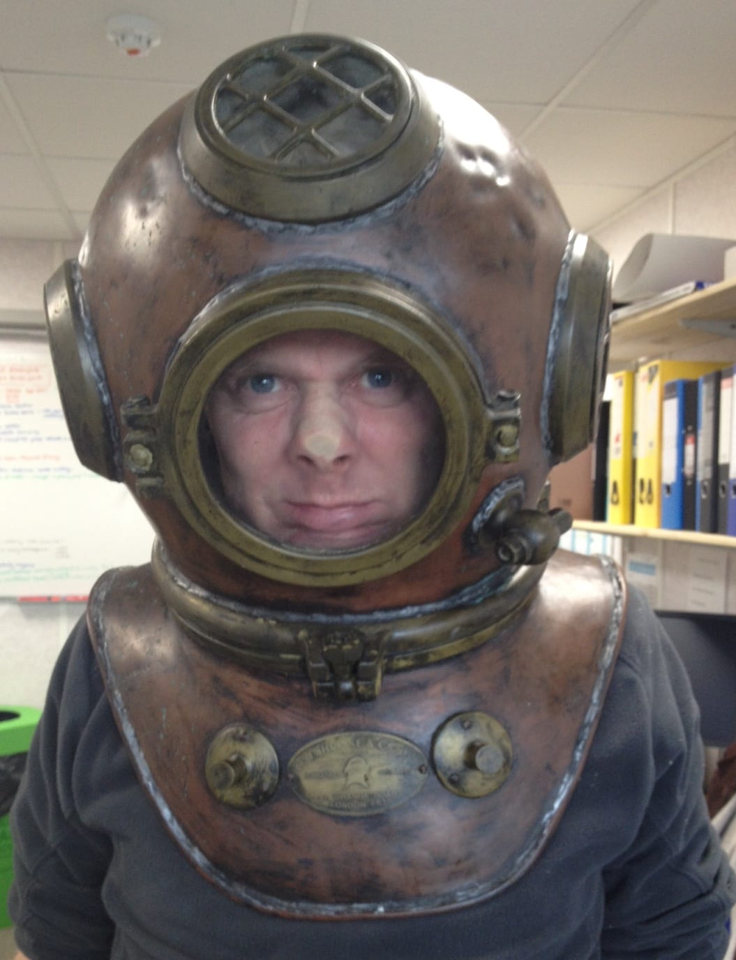 DDRC CEO Dr Gary Smerdon with his head inside a smelly old diving helmet. His nose is squashed against the inside of the glass and his expression shows this is not pleasurable. 