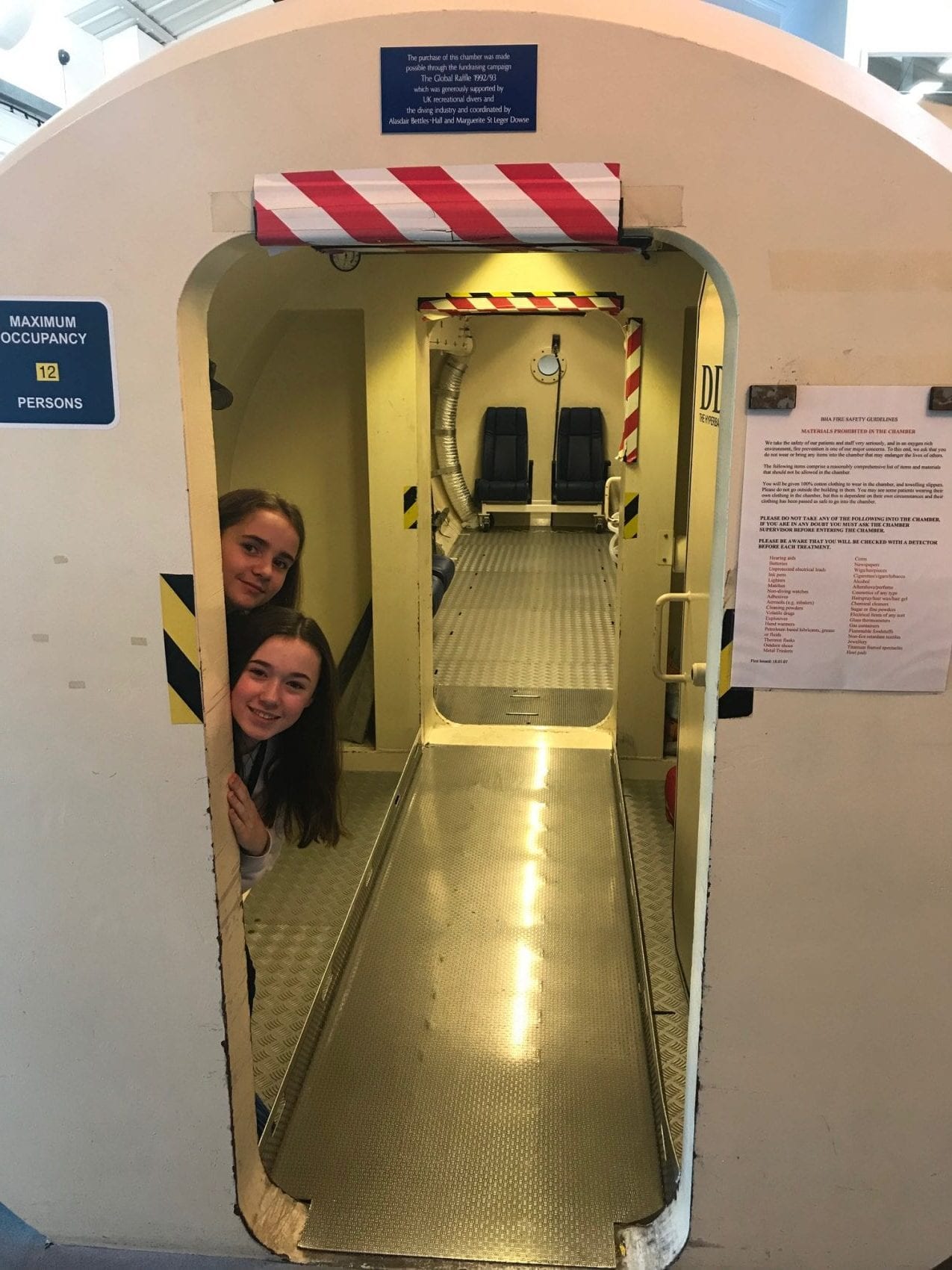 Fundraising girls peering around the door of the Krug hyperbaric chamber